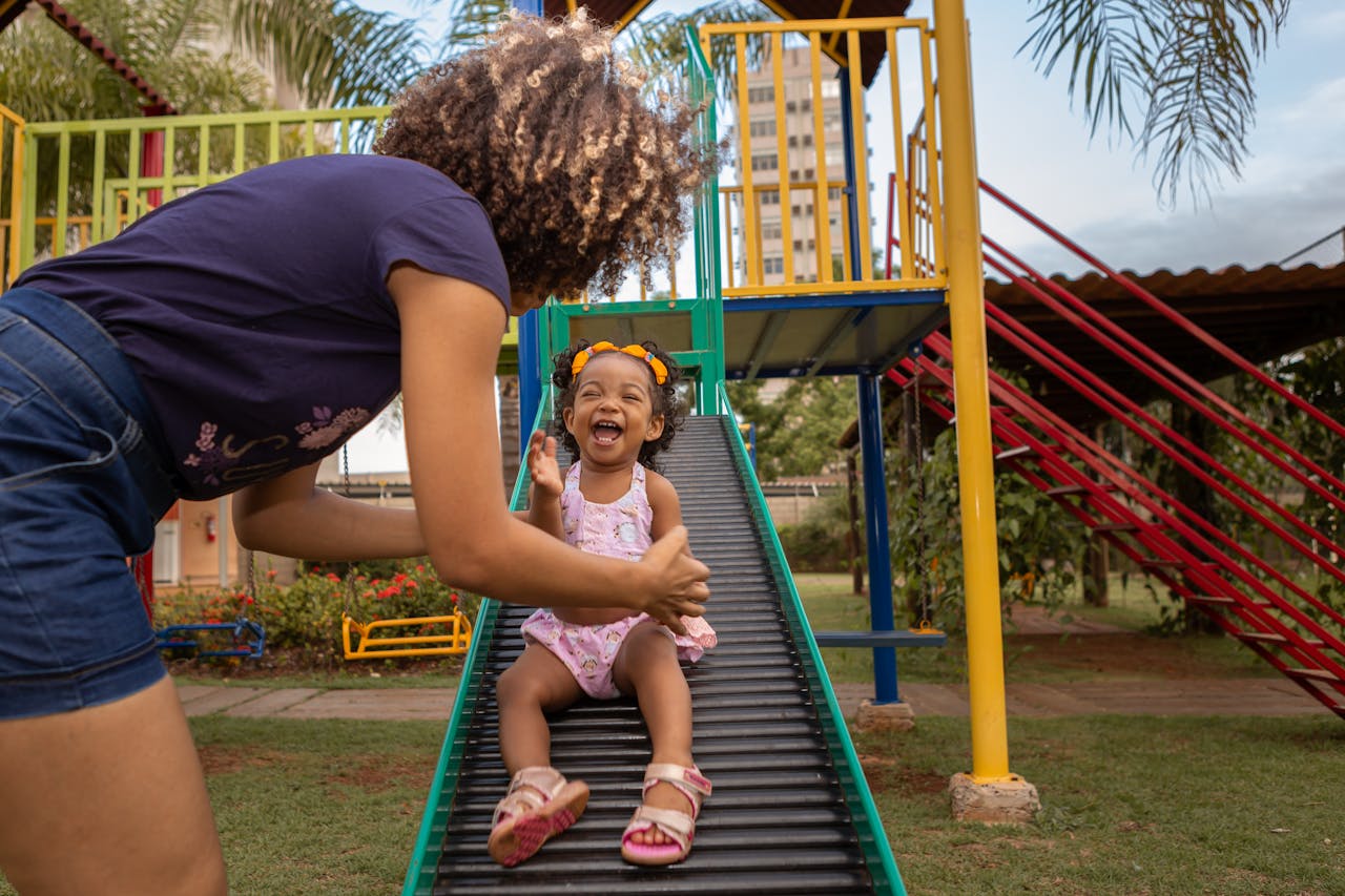 Happy mother and daughter enjoying time at an outdoor playground slide.